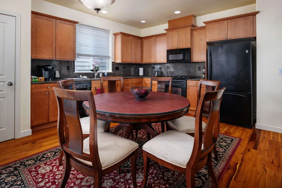 A round dining table set atop a decorative rug, surrounded by kitchen cabinetry and black appliances. The space is designed for intimate family meals, casual gatherings, and entertaining.